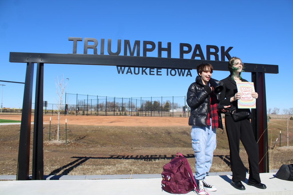 two students stand infront of a Triumph Park sign while speaking